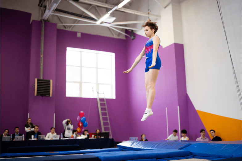 Девочка в спортивной форме демонстрирует прыжки на батуте судьям